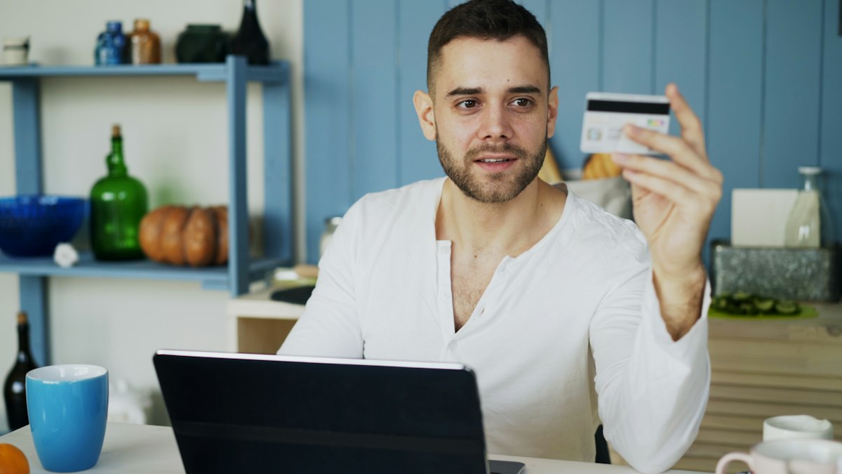 Online shopper holding a credit card up to a laptop during checkout